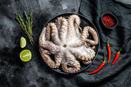Raw octopus in a plate with cooking ingredients. Black background. Top view.の写真素材