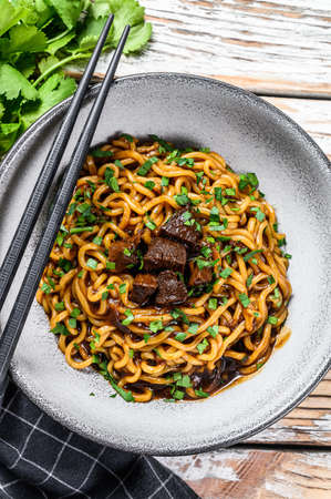 Instant ramen noodles with coriander and tofu in a cast-iron pot. Vegetarian dish. White wooden background. Top view