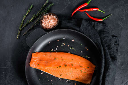 Raw trout fillet with salt and chili pepper in a pan. Organic fish. Black background. Top view