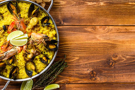 The Spanish paella with seafood prawns, shrimps, mussels in a paellera. Wooden background. Top view. Copy space.の写真素材