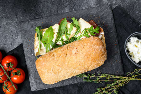 Ciabatta sandwich with fresh goat cheese, pear marmalade and arugula. Black background. Top view.の写真素材