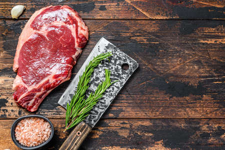 Raw cowboy or rib eye steak on the bone on a meat cleaver. Marble beef meat ribeye. Dark wooden background. Top view. Copy space.の写真素材