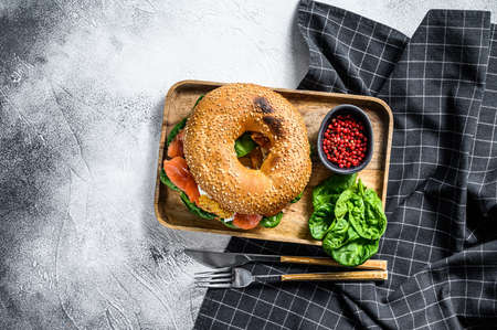 Bagel sandwich with salmon, cream cheese, spinach and egg on a wooden plate. Gray background. Top view.の写真素材
