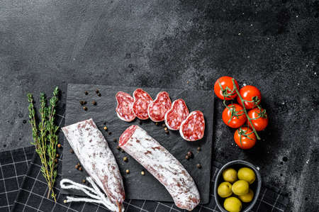 Fuet Salami cut in slices and Rosemary. Traditional Spanish sausage. Black background. Top view....