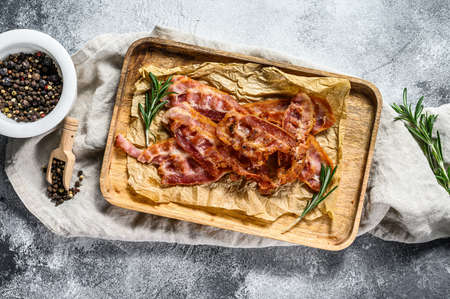Fried bacon on a wooden chopping Board. Serve with rosemary and black pepper. Gray background. Top viewの写真素材