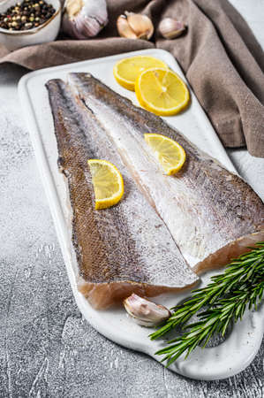 Fresh raw hake fish fillet with pepper and lemon. White background. Top view.