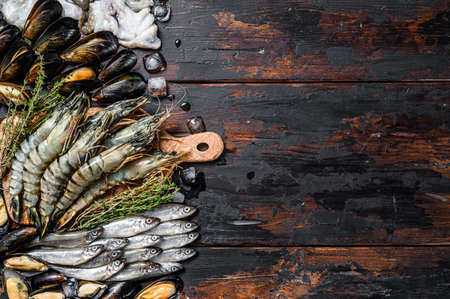 Assorted set of fresh seafood tiger prawns, shrimps, blue mussels, octopuses, sardines, smelt. Dark woodden background. Top view. Copy space.の写真素材