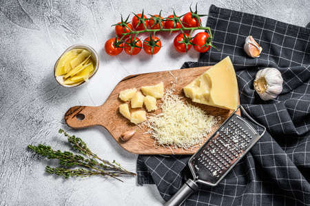 Grated parmesan cheese and metal grater on wooden cutting board. Gray background. Top view.