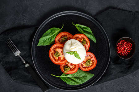 Burrata cheese and tomatoes salad served on black plate. Dark background. Top view.の写真素材
