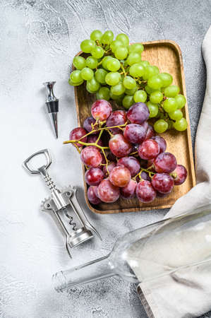 Wine background. A branch of green and red grapes, an empty bottle, a corkscrew and a cork. Concept of home winemaking. White background. Top view.の写真素材