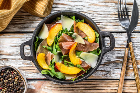 Salad with jamon Iberico, arugula, peach and Parmesan in a iron pan. White background. Top view.の写真素材