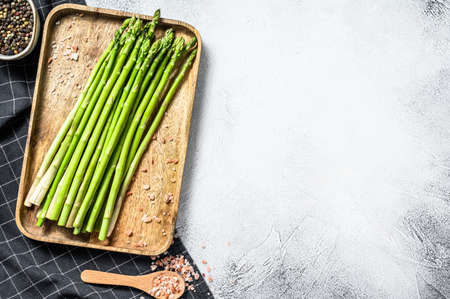 Fresh baby green asparagus in a wooden bowl. White background. Top view. Copy space.の写真素材