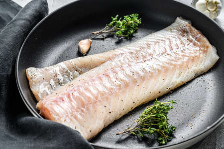 Raw cod loin with herbs in a frying pan. Gray background. Top view.