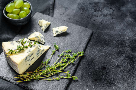 Triangle of blue cheese with grapes on cutting board. Black background. Top view. Copy space.