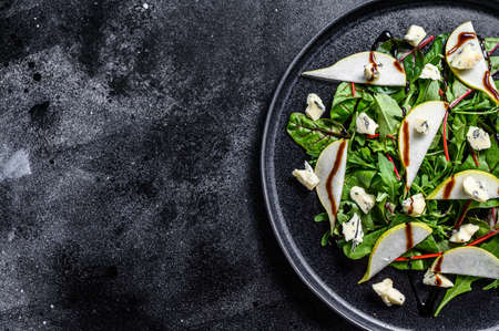 Pear, blue cheese, arugula and nut salad on plate. Black background. Top view. Copy space.の写真素材