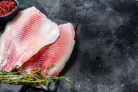 Fresh tilapia fillet on a chopping Board with thyme. Black background. Top view. Copy space.の写真素材