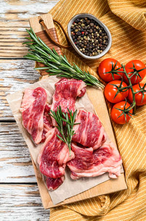 Strips of marbled beef, quick steak on cutting board. White wooden background. Top view.の写真素材