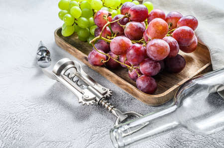 Wine background. A branch of green and red grapes, an empty bottle, a corkscrew and a cork. Concept of home winemaking. White background. Top view.の写真素材