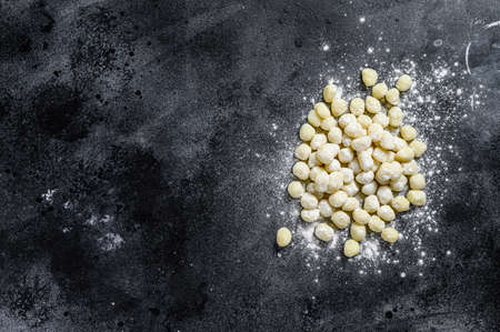 Uncooked homemade gnocchi on black cutting board. Black background. Top view. Copy spaceの写真素材