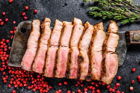 Grilled sliced pork steak on a meat cleaver. Organic meat. Black background. Top view.