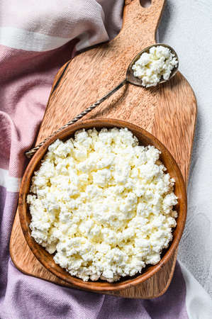 Fresh Cottage cheese in a wooden bowl on cutting board. Gray background. Top view.