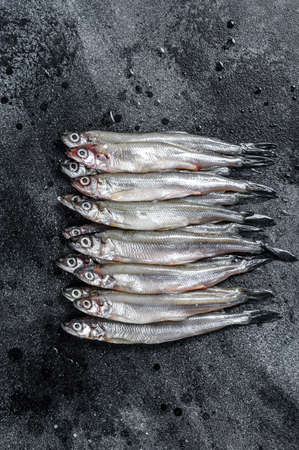 Fresh raw sea small fish smelt. Black background. Top view.