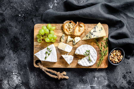 Cheese plate with Camembert, brie and blue cheese with grapes and walnuts. Black background. Top...