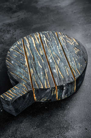Old dark cutting board on brown wooden table. Black background. Top view. Copy space.の写真素材
