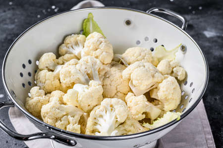 Washed fresh cauliflower cut into pieces in a colander. Black background. Top view.の写真素材