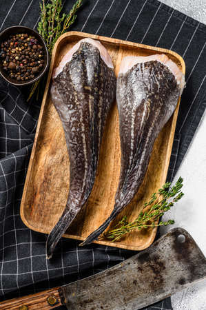Raw monkfish on a wooden tray with a cleaver. Gray background. Top view.