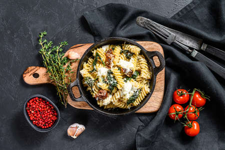 Fusilli pasta with spinach, dried tomatoes and ricotta cheese ia a pan. Black background. Top view.の写真素材