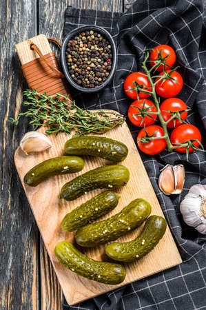 Marinated pickled cucumbers with herbs and spices on cutting board. Black background. Top view.の写真素材