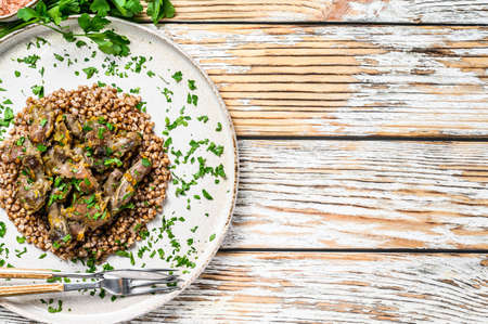 Stewed chicken stomachs with vegetables and buckwheat on a plate. Wooden white background. Top view. Copy space.の写真素材