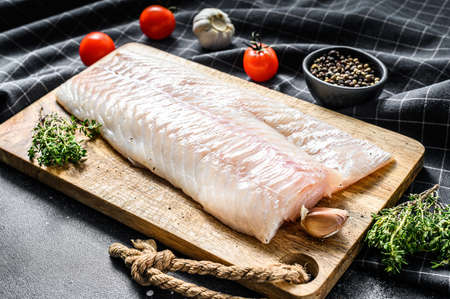 Raw cod fillet with and herbs on rustic wooden cutting board. Black background. Top view.の写真素材