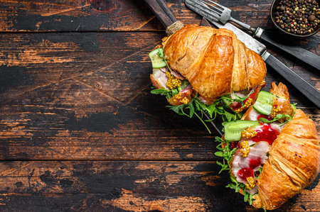 Croissant filled with ham and lettuce on wooden chopping board. Black background. Top view. Copy space.の写真素材