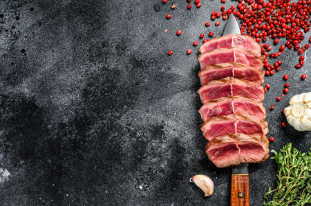 Sliced ready to eat steak Top Blade beef breeds, black Angus meat. Black background. Top view. Copy...
