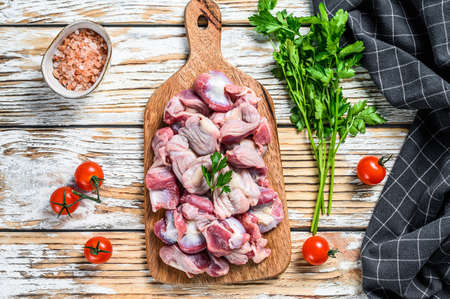 Raw uncooked Bird chicken giblets gizzards, stomachs on a cutting board. wooden background. Top...