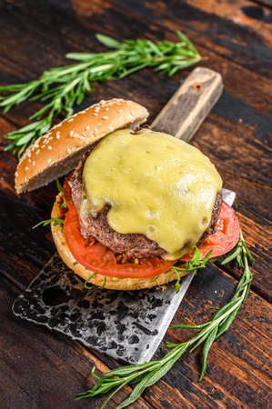 Grilled homemade burger with beef, tomato, cheese, cucumber and lettuce on a meat cleaver. Dark wooden background. Top view.の写真素材