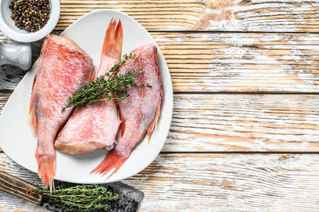 Whole raw red perch or sea bass fish on a plate. White wooden background. Top view. Copy space.