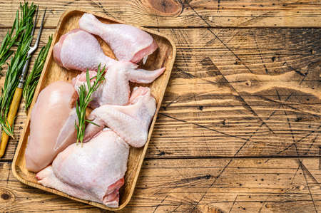 Fresh raw chicken meat, wings, breast, thigh and drumsticks on a wooden tray. Wooden background. Top view. Copy space.の写真素材