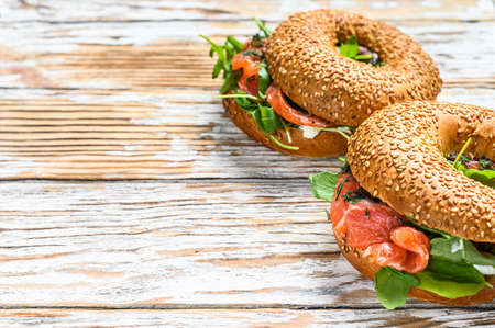 Bagels with salmon, cream, avocado and arugula. White wooden background. Top view. Copy space.