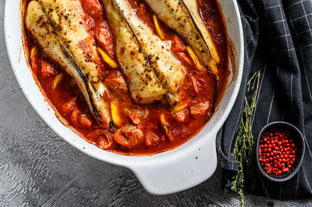 Monkfish baked in tomatoes in a baking dish. Black background. Top view.