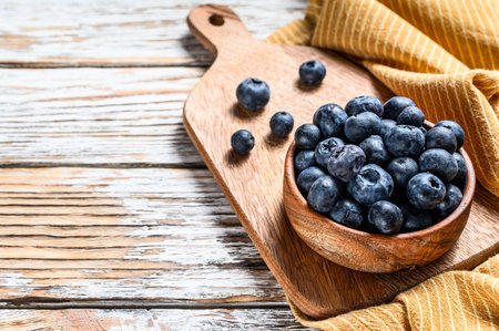 Ripe blueberries in a wooden bowl. White wooden background. Top view. Copy space.の写真素材