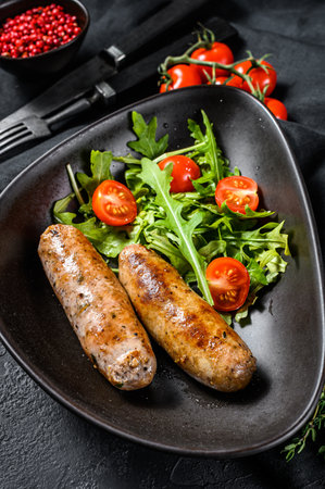 Grilled pork sausages with tomato and arugula salad. Black background. Top view.の写真素材