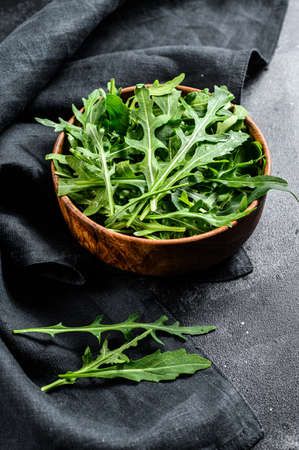 Fresh arugula in a wooden bowl. Black background. Top view.の写真素材
