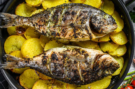 Grilled Dorado fish with potatoes in a pan. Gray background. top view.