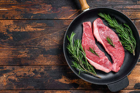 Raw beef meat rump steak in a pan. Dark wooden background. Top view. Copy space.の写真素材