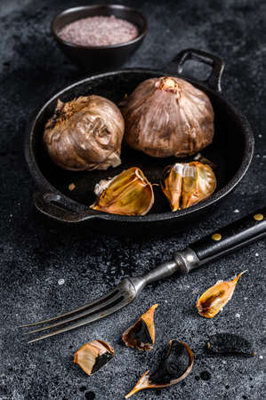 Bulbs of fermented black garlic in a pan. Black background. Top view.の写真素材