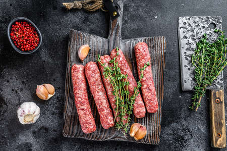 Fresh raw beef meat kebabs sausages on a cutting board. Black background. Top view.の写真素材