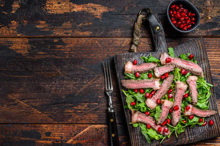 Grilled Beef Steak salad with arugula, pomegranate and greens vegetables. Dark wooden background. Top view. Copy space.の写真素材